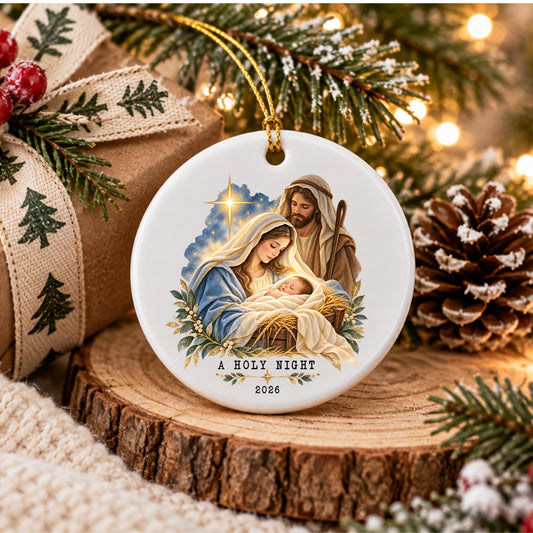May include: A round white ceramic Christmas ornament featuring a colorful illustration of the Nativity scene with Mary, Joseph, and the baby Jesus. The text A HOLY NIGHT and the year 2026 are printed in black at the bottom of the ornament.