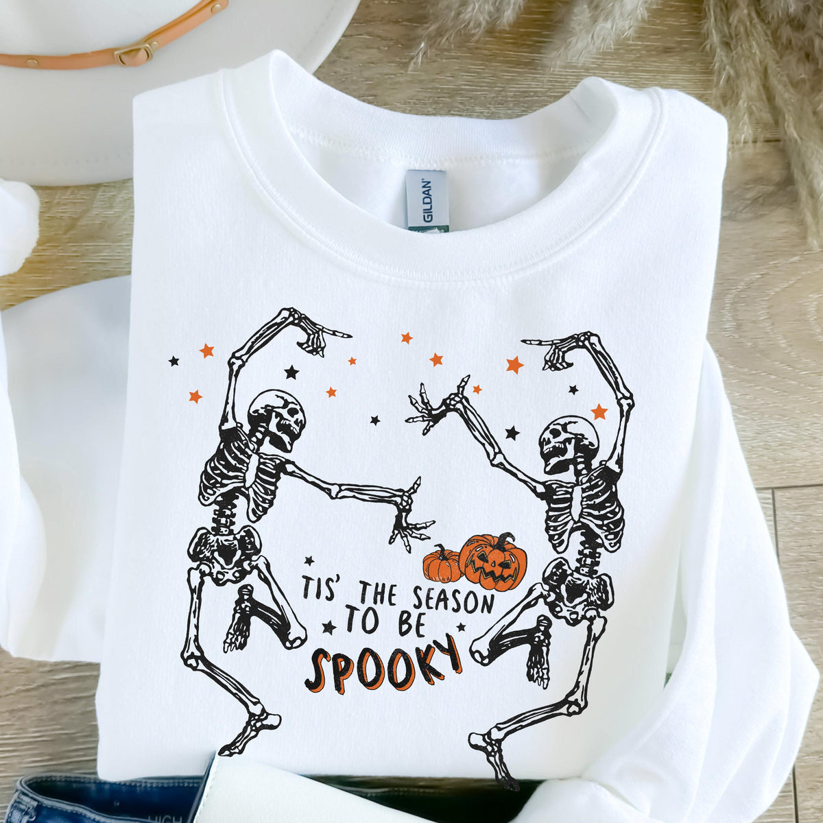 May include: White sweatshirt featuring a Halloween design. The graphic includes two dancing skeletons, orange stars, and pumpkins. Text reads "Tis' the season to be spooky."