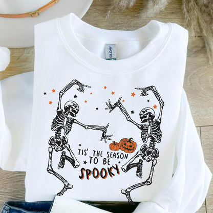 May include: White sweatshirt featuring a Halloween design. The graphic includes two dancing skeletons, orange stars, and pumpkins. Text reads "Tis' the season to be spooky."