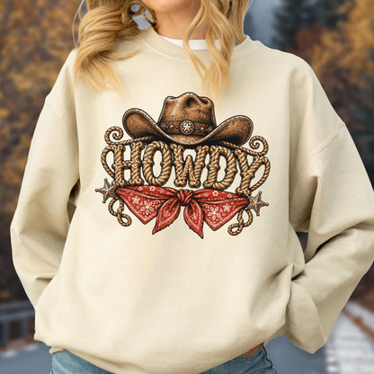 May include: A cream-colored crewneck sweatshirt featuring a graphic print of a brown cowboy hat above the word HOWDY written in a rope-style font. Below the text is a red bandana with a white floral pattern and two small silver stars.