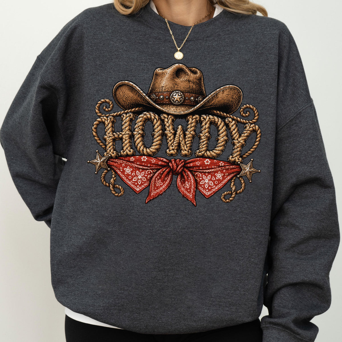 May include: A dark charcoal gray crewneck sweatshirt featuring a graphic print of a brown cowboy hat above the word HOWDY written in a rope-textured font, with a red paisley bandana and two small metallic stars positioned below the text.