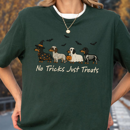 May include: A dark green t-shirt featuring a graphic of four dachshunds in Halloween costumes, including a witch, a mummy, a ghost holding a pumpkin bucket, and a skeleton. The text "No Tricks Just Treats" is printed below the dogs.