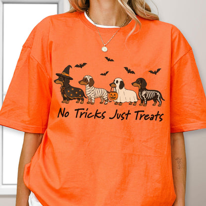 May include: An orange t-shirt featuring a graphic of four dachshunds in Halloween costumes, including a witch, a mummy, a ghost, and a skeleton, with bats above and the text "No Tricks Just Treats" printed in black lettering below the dogs.