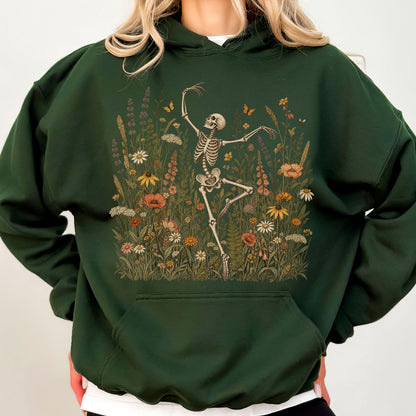 May include: A dark forest green hooded sweatshirt featuring a graphic print of a white skeleton dancing amidst a field of colorful wildflowers, including orange, yellow, and white blossoms, with a large front kangaroo pocket and long sleeves.