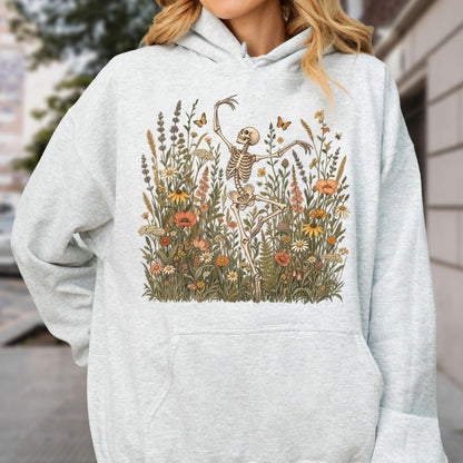 May include: A light gray heathered hooded sweatshirt featuring a central graphic print of a human skeleton dancing amidst a dense field of colorful wildflowers, tall grasses, and small butterflies in shades of orange, yellow, and muted green.