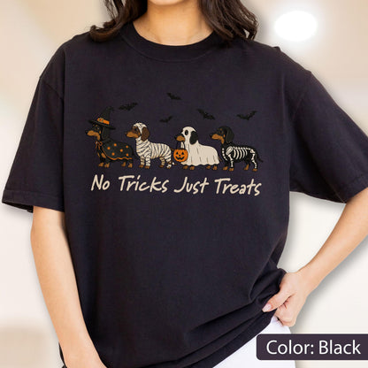 May include: A black short-sleeved t-shirt featuring a graphic of four dachshunds in Halloween costumes, including a witch, a mummy, a ghost holding a pumpkin bucket, and a skeleton. The text "No Tricks Just Treats" is printed below the dogs.
