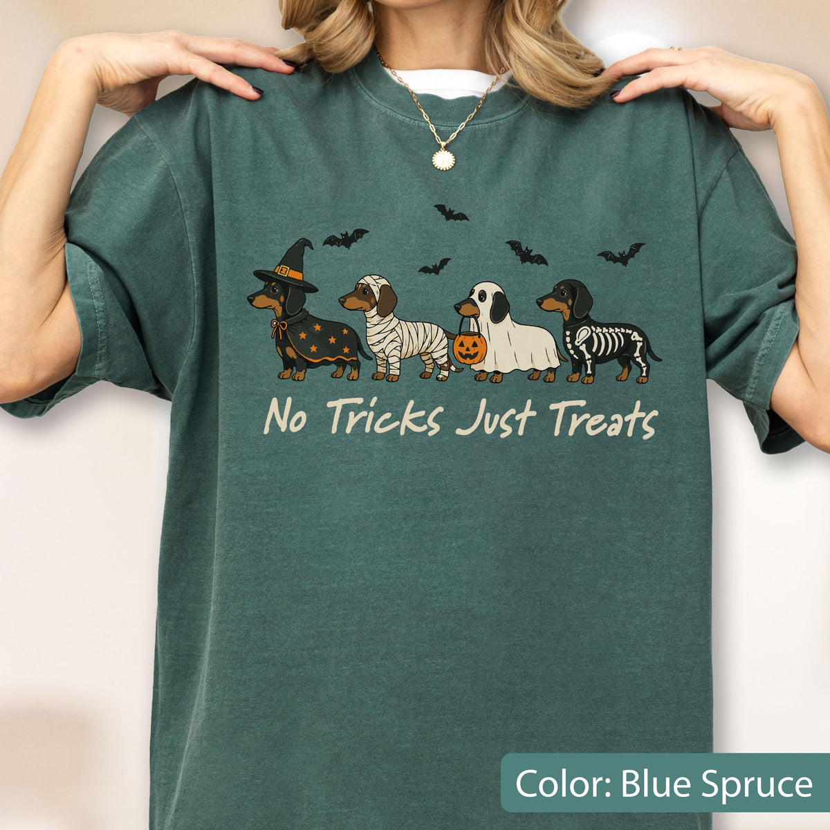 May include: A blue spruce crewneck t-shirt featuring a graphic of four dachshunds in Halloween costumes, including a witch, mummy, ghost, and skeleton. The text "No Tricks Just Treats" is printed below the dogs, accompanied by small black bats.