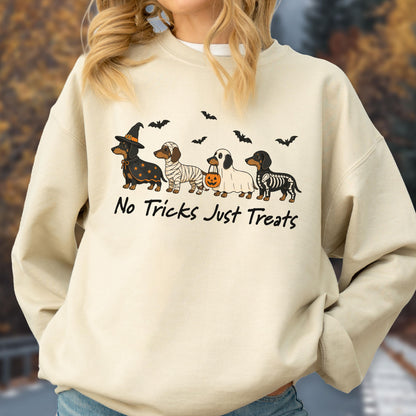 May include: A beige crewneck sweatshirt featuring a graphic of four dachshunds in Halloween costumes, including a witch, mummy, ghost, and skeleton. The text "No Tricks Just Treats" is printed below the dogs, accompanied by small black bats.