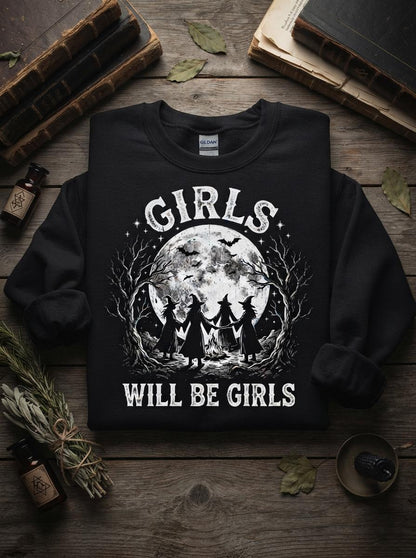 May include: A black crewneck sweatshirt featuring a white graphic print of four witches holding hands around a campfire under a large full moon. The text GIRLS is printed above the moon and WILL BE GIRLS is printed below the graphic in a distressed font.