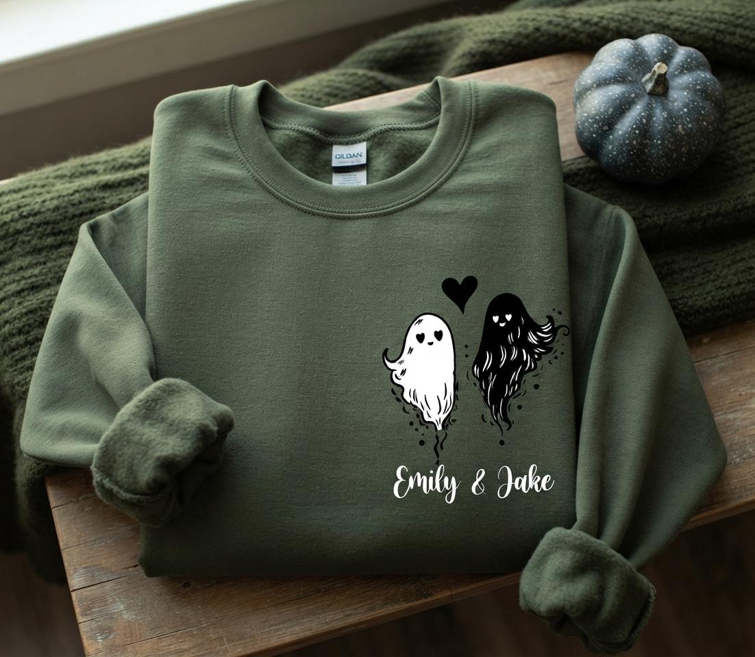May include: An olive green crewneck sweatshirt featuring a graphic of two ghosts, one white and one black, with heart-shaped eyes. A small black heart is positioned between the ghosts, and the text "Emily & Jake" is printed below in white.