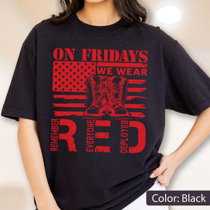 May include: A black t-shirt featuring a red graphic of an American flag with a pair of combat boots in the center. The text reads ON FRIDAYS WE WEAR RED and REMEMBER EVERYONE DEPLOYED in a distressed, bold, block-style red font.