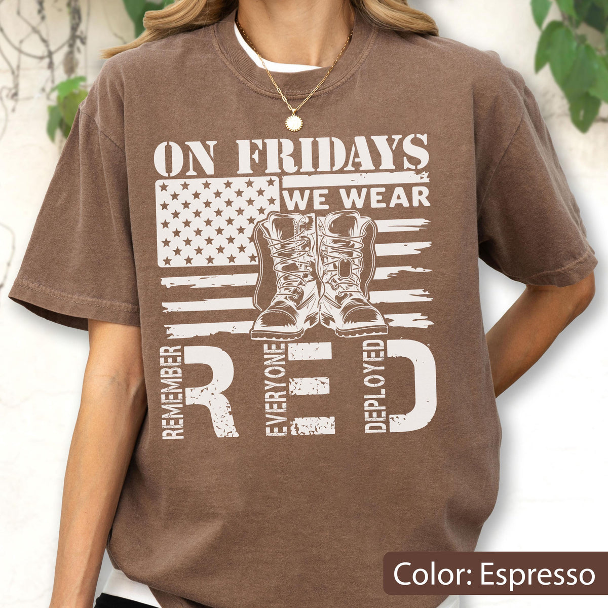 May include: An espresso brown short-sleeve t-shirt featuring a white graphic print of an American flag, a pair of military boots, and the text ON FRIDAYS WE WEAR RED REMEMBER EVERYONE DEPLOYED. The shirt has a crew neckline and a relaxed fit.