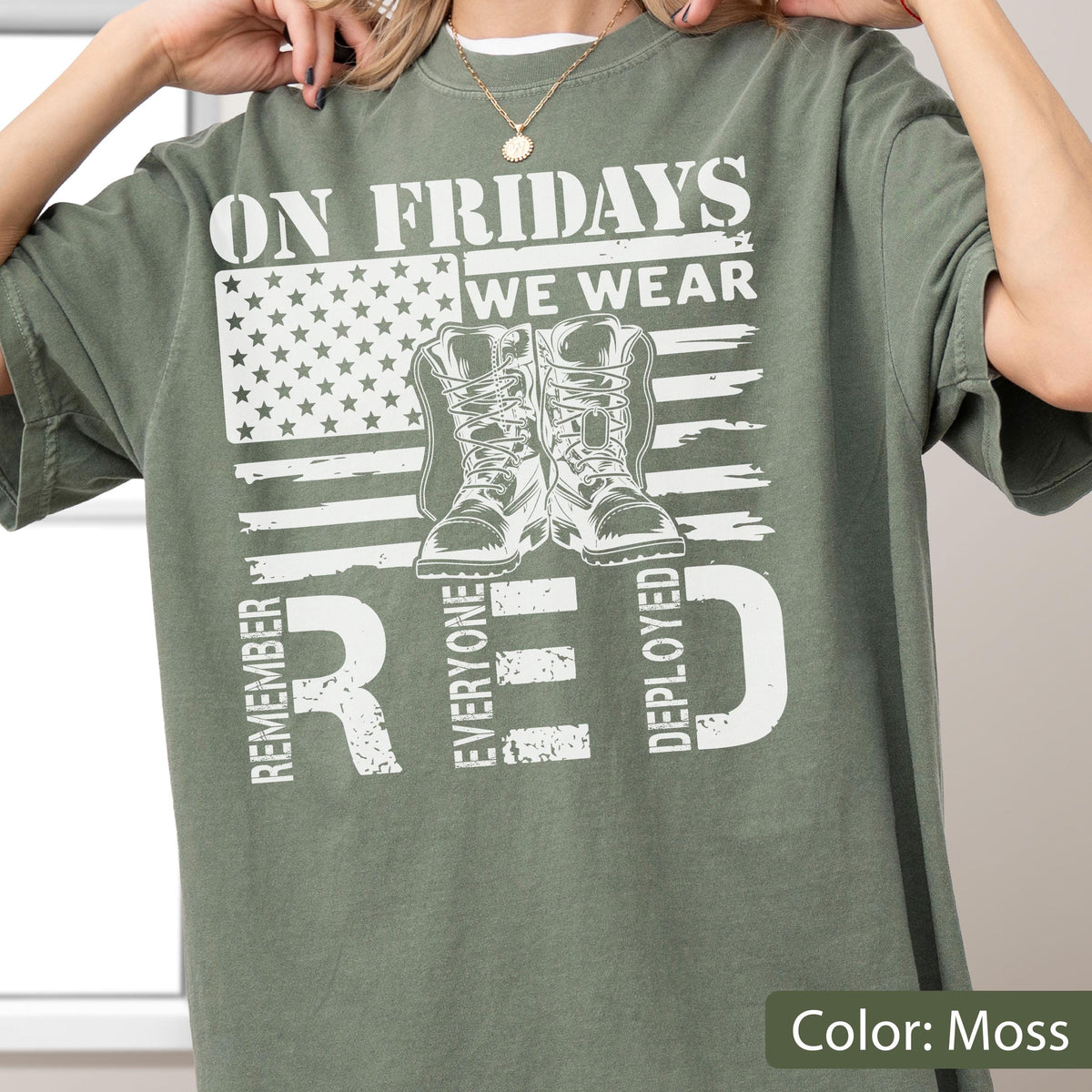 May include: A moss green t-shirt featuring a white graphic print of an American flag, a pair of military boots, and the text ON FRIDAYS WE WEAR RED REMEMBER EVERYONE DEPLOYED. The shirt has a crew neckline and short sleeves with a relaxed fit.