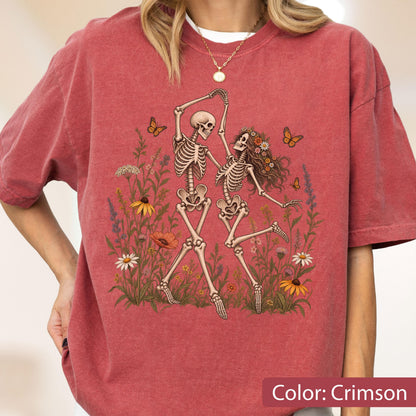 May include: A crimson short-sleeve t-shirt featuring a graphic print of two skeletons dancing in a field of colorful wildflowers and butterflies. The design includes various floral elements in shades of yellow, orange, and white, with orange butterflies.