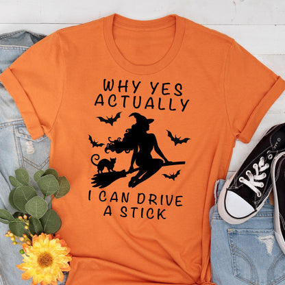 May include: Orange t-shirt with the text "WHY YES ACTUALLY I CAN DRIVE A STICK" and a black silhouette of a witch on a broom, a black cat, and bats. The shirt is folded at the sleeves.