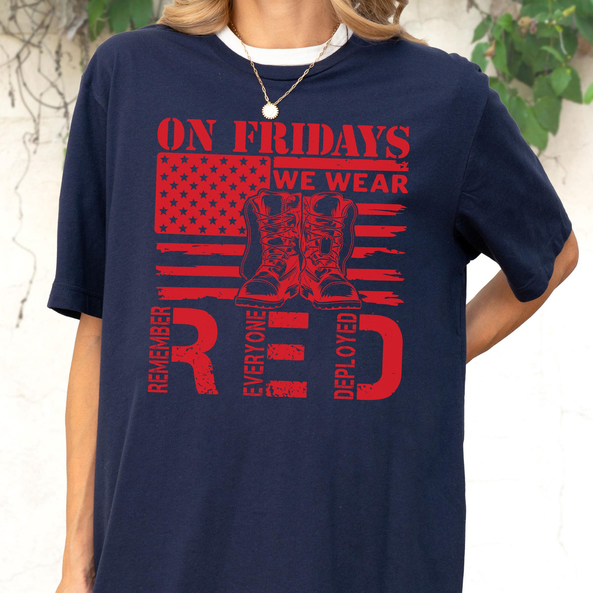 May include: A navy blue t-shirt featuring a red graphic print of a stylized American flag and a pair of military boots. The text reads ON FRIDAYS WE WEAR RED and REMEMBER EVERYONE DEPLOYED in a distressed, bold, red font across the chest area.