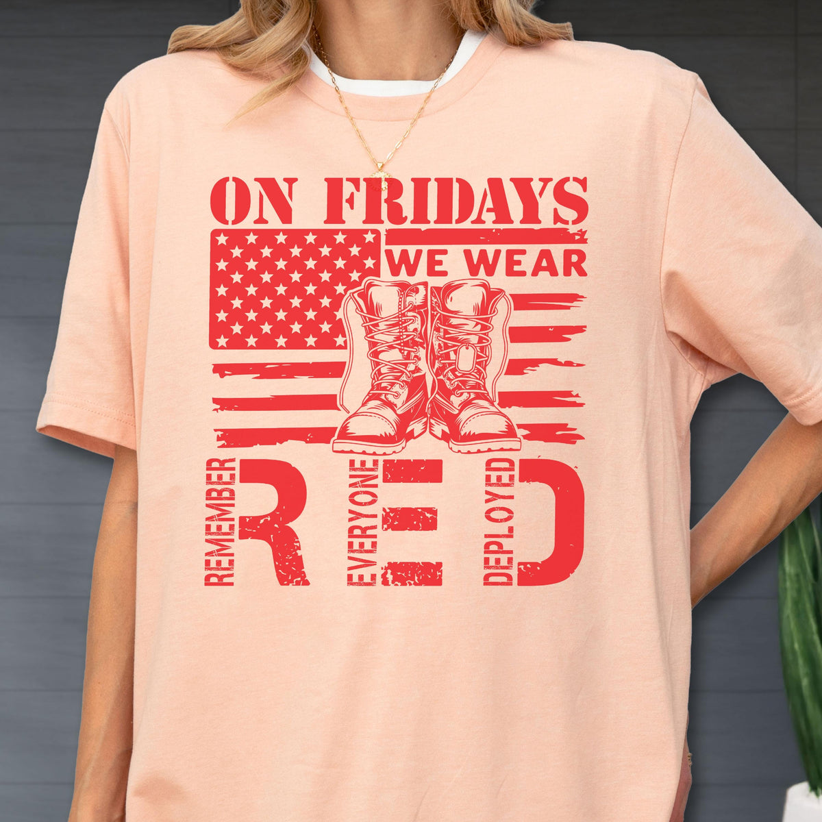 May include: A peach-colored t-shirt featuring a red graphic of an American flag and a pair of military boots. The text reads ON FRIDAYS WE WEAR RED and REMEMBER EVERYONE DEPLOYED, with the letters R, E, and D enlarged at the bottom of the design.