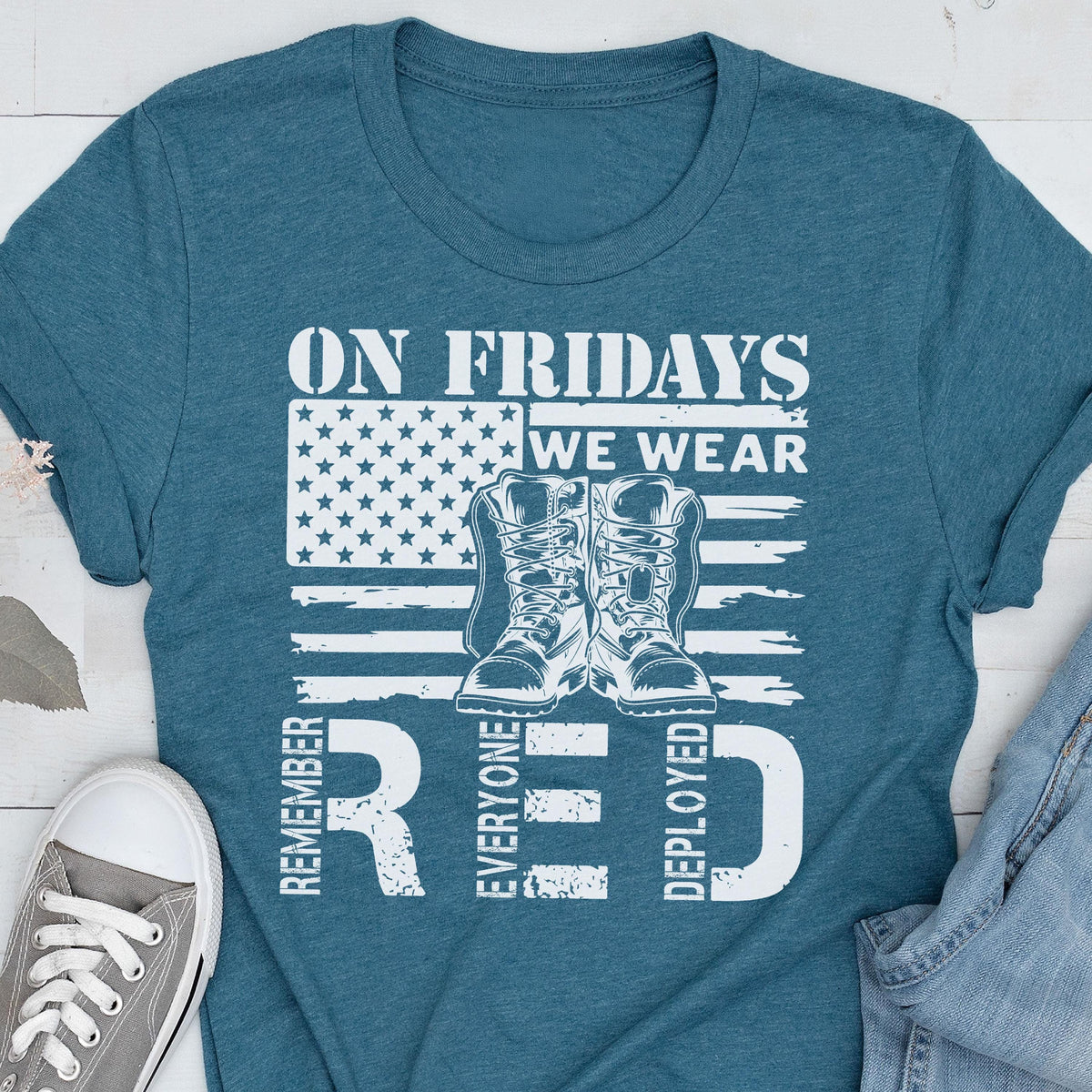 May include: A teal short-sleeved t-shirt featuring a white graphic of an American flag, a pair of military boots, and the text: ON FRIDAYS WE WEAR RED REMEMBER EVERYONE DEPLOYED. The design is centered on the chest of the shirt.
