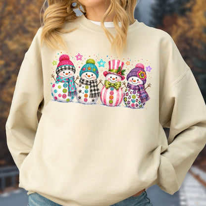May include: A beige crewneck sweatshirt featuring a graphic of four snowmen. The snowmen wear colorful hats, scarves, and patterned accessories, including a top hat and bow tie. The design is accented with small colorful stars and dots.