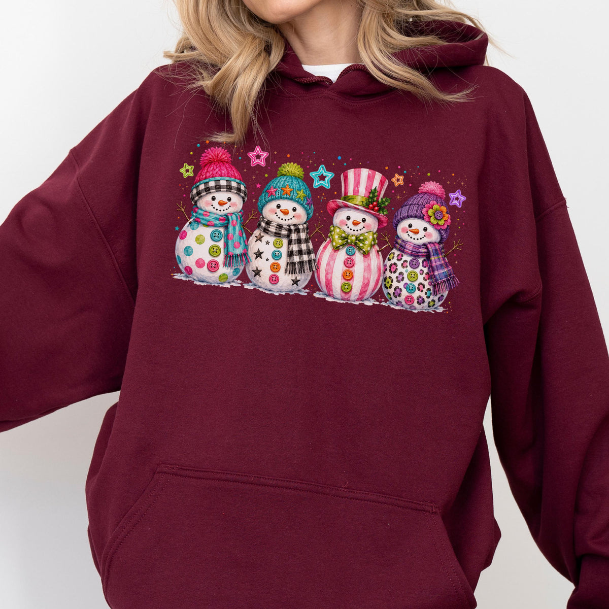 May include: A maroon hooded sweatshirt featuring a graphic print of four snowmen. Each snowman wears a colorful hat and scarf, with button-like details on their bodies. The design includes small, multi-colored stars scattered above the snowmen.