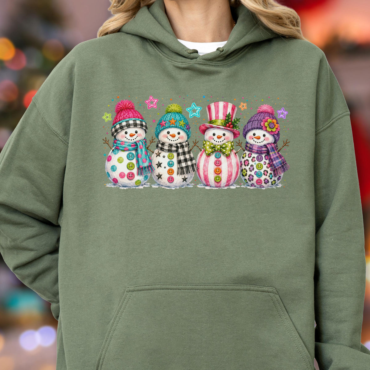 May include: An olive green hooded sweatshirt featuring a graphic print of four snowmen standing in a row. Each snowman wears a colorful hat and scarf, with buttons on their bodies and small star shapes floating in the background above them.