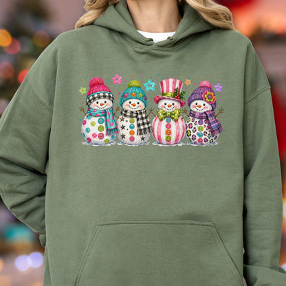 May include: An olive green hooded sweatshirt featuring a graphic print of four snowmen standing in a row. Each snowman wears a colorful hat and scarf, with buttons on their bodies and small star shapes floating in the background above them.