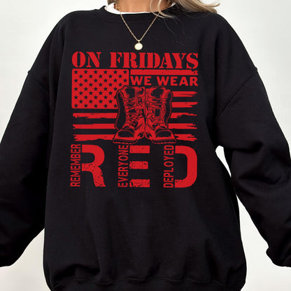 May include: A black crewneck sweatshirt featuring a red graphic print of a stylized American flag and a pair of military boots. The text reads ON FRIDAYS WE WEAR RED and REMEMBER EVERYONE DEPLOYED in a bold, distressed red font across the chest.
