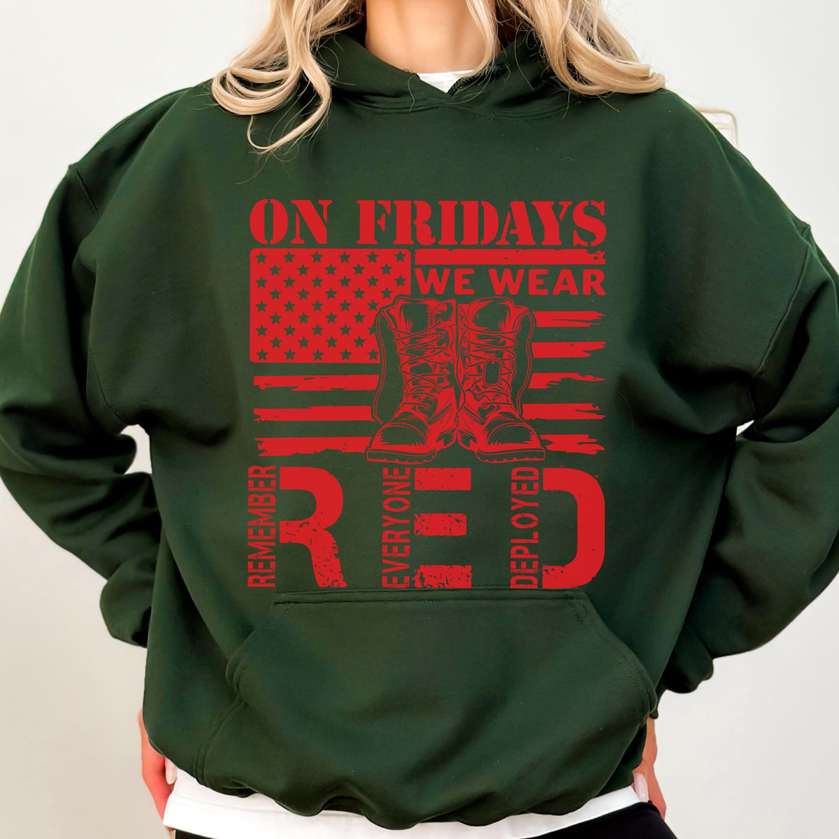 May include: A dark green hooded sweatshirt featuring a red graphic print. The design includes a stylized American flag, a pair of military boots, and the text ON FRIDAYS WE WEAR RED REMEMBER EVERYONE DEPLOYED in a bold, distressed red font.