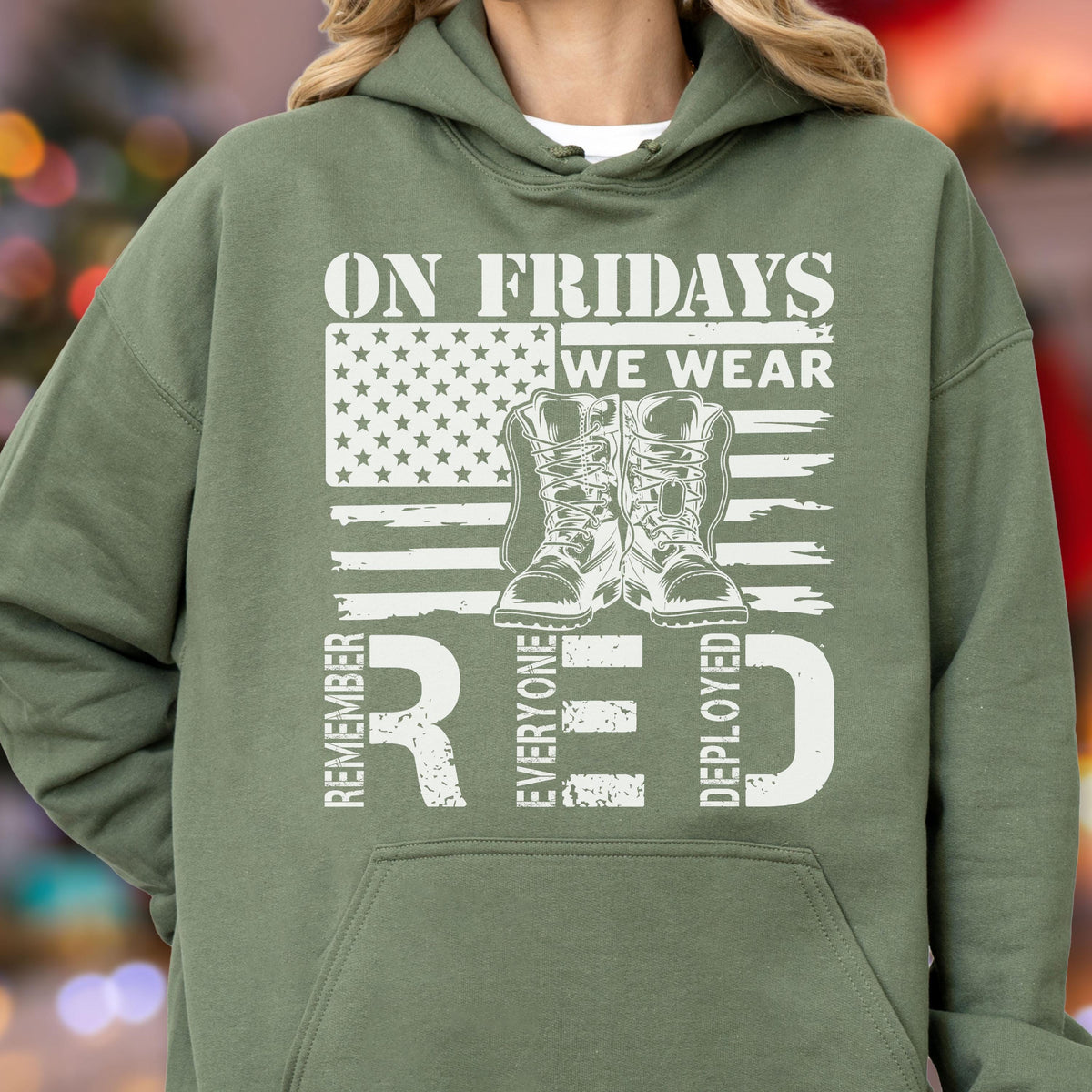 May include: An olive green hooded sweatshirt featuring a white graphic print of an American flag, a pair of military boots, and the text ON FRIDAYS WE WEAR RED REMEMBER EVERYONE DEPLOYED. The hoodie includes a front kangaroo pocket and long sleeves.