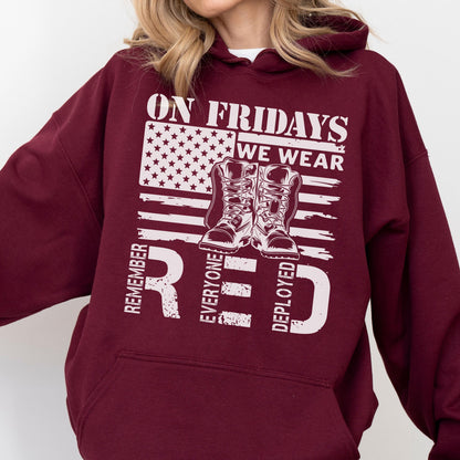 May include: A maroon hooded sweatshirt featuring a white graphic print of the American flag, a pair of military boots, and the text ON FRIDAYS WE WEAR RED REMEMBER EVERYONE DEPLOYED. The hoodie includes a front kangaroo pocket and long sleeves.