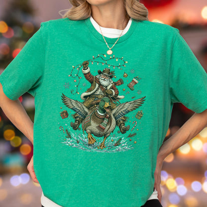 May include: A bright green short-sleeved t-shirt featuring a graphic illustration of Santa Claus wearing a cowboy hat and riding a flying mallard duck. The design includes festive elements like Christmas lights, snowflakes, and gifts.
