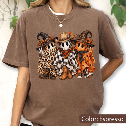 May include: An espresso-colored t-shirt featuring a graphic of three ghosts wearing hats. The left ghost has a leopard print sheet, the middle ghost has a black and white checkered sheet with a cowboy hat, and the right ghost has an orange polka dot sheet.