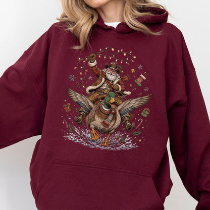May include: A maroon hooded sweatshirt featuring a graphic print of Santa Claus riding a flying mallard duck. The design includes Christmas lights, snowflakes, wrapped gifts, and candy canes surrounding the central figures on the front of the garment.