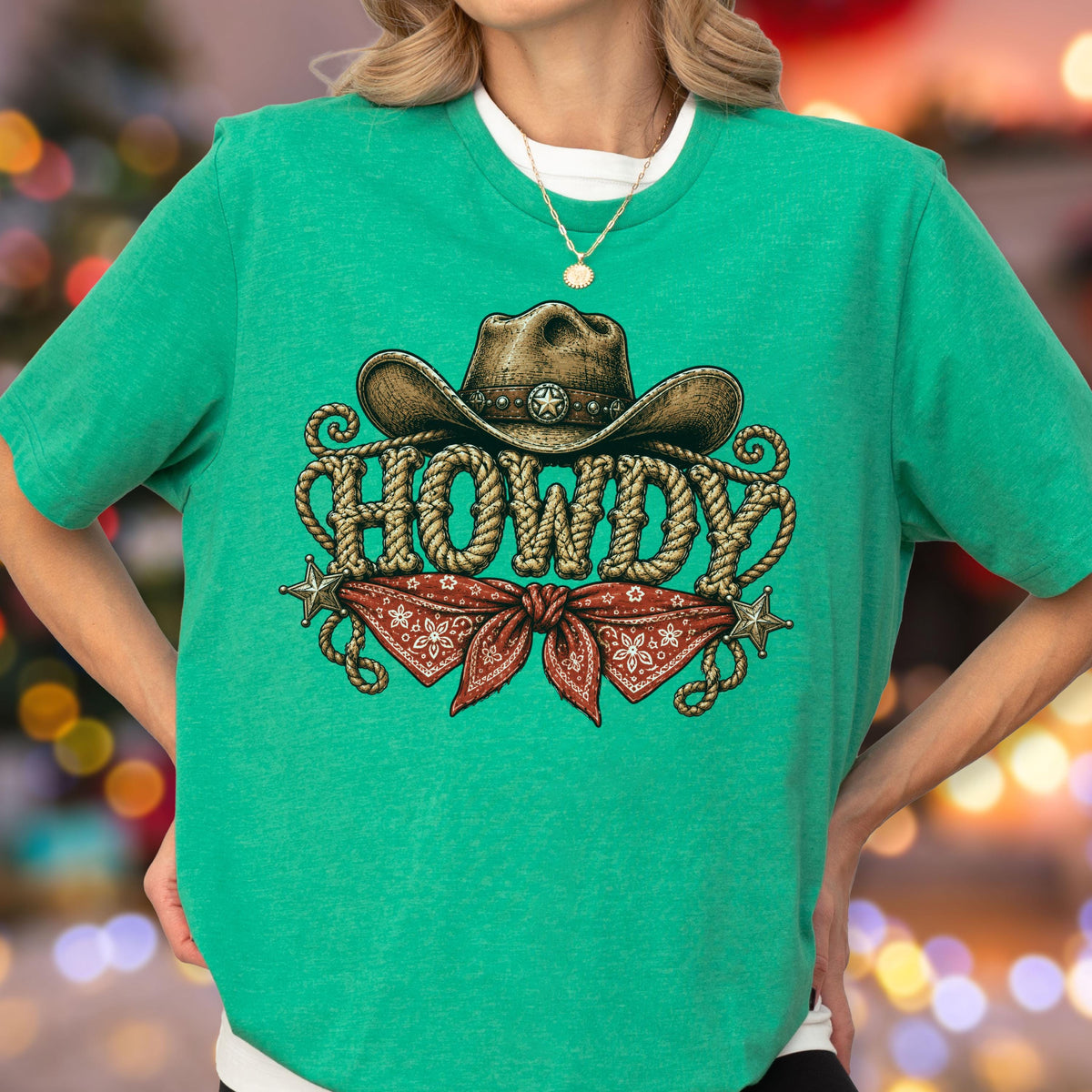 May include: A bright green short-sleeve t-shirt featuring a graphic print of a brown cowboy hat above the word HOWDY written in a rope-style font. Below the text is a red bandana with a white pattern, flanked by two small silver stars.