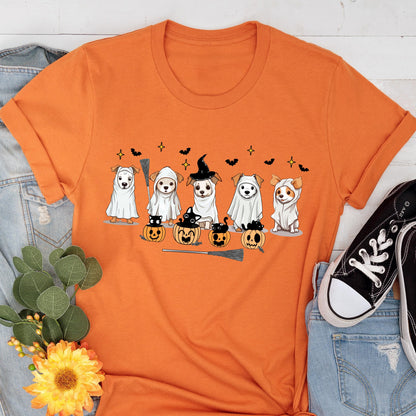 May include: An orange short-sleeved t-shirt featuring a graphic print of five dogs in white ghost costumes, some wearing witch hats, alongside small black cats sitting in carved orange pumpkins, with black bats and yellow stars in the background.