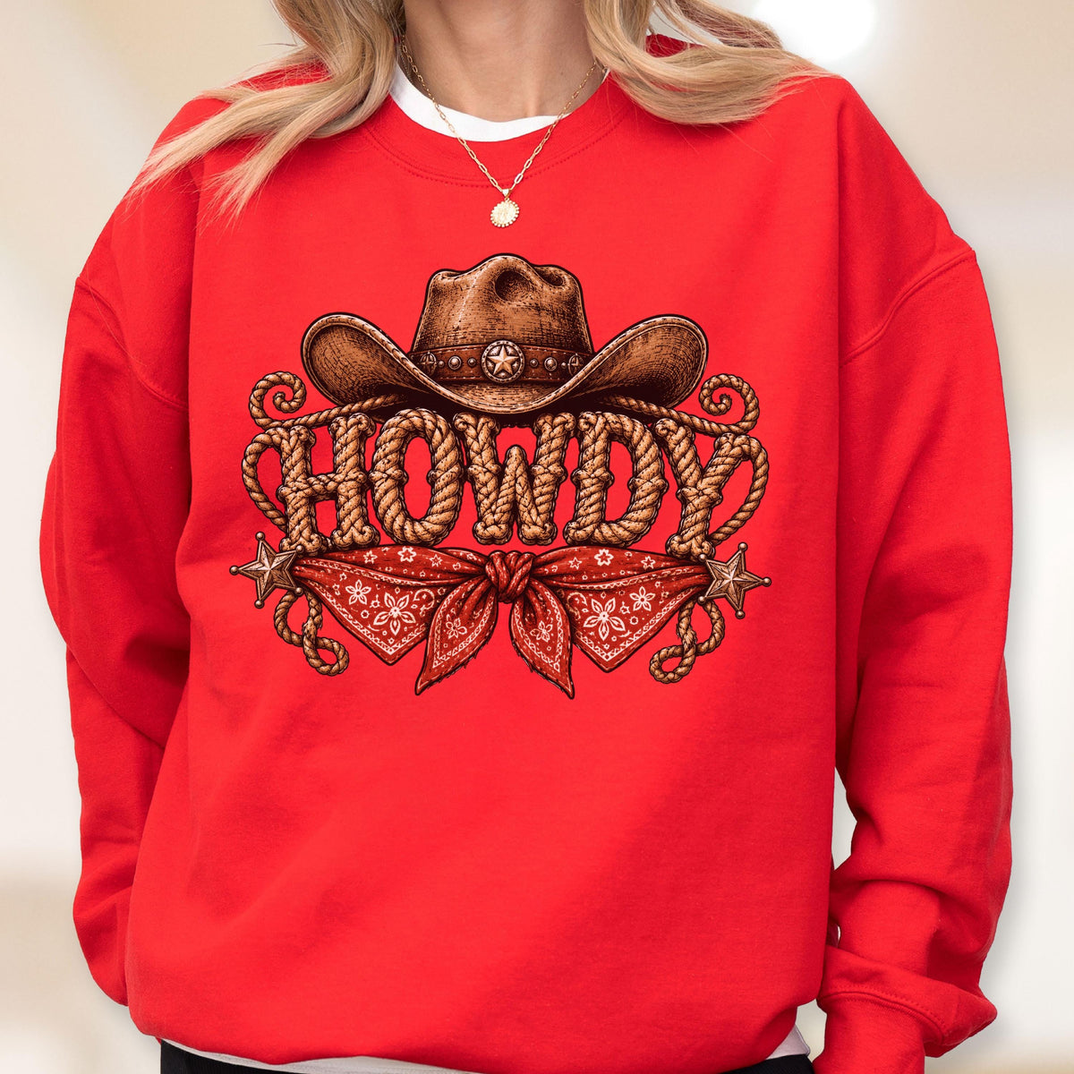 May include: A bright red crewneck sweatshirt featuring a graphic print of a brown cowboy hat, a red bandana, and the word HOWDY written in a rope-style font. The design includes two small star accents on the left and right sides of the graphic.