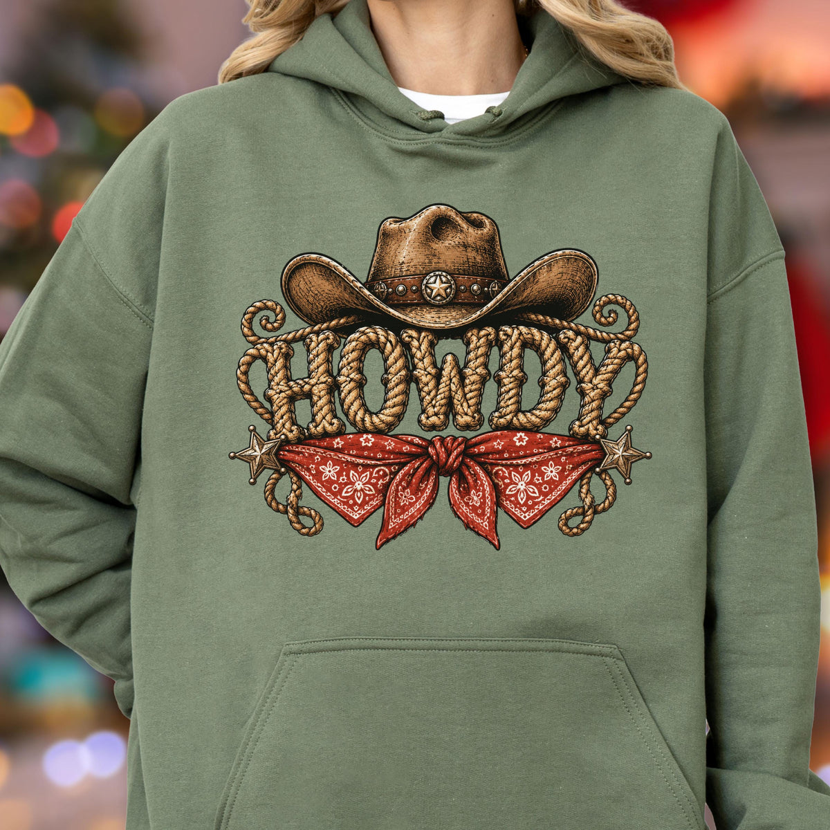 May include: An olive green hooded sweatshirt featuring a graphic print of a brown cowboy hat above the word HOWDY, which is written in a rope-style font. Below the text is a red bandana with a white pattern and two small star accents.