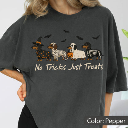 May include: A charcoal gray t-shirt featuring a graphic of four dachshunds in Halloween costumes, including a witch, a mummy, a ghost with a pumpkin bucket, and a skeleton. Above the dogs are black bats, and below is the text No Tricks Just Treats.