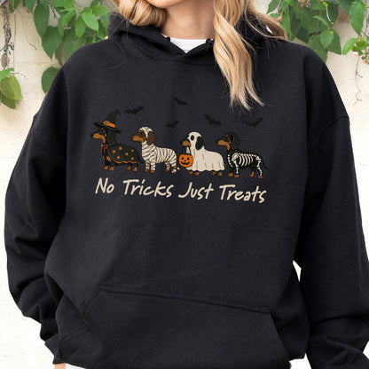 May include: A black hooded sweatshirt featuring a graphic of four dachshunds in Halloween costumes, including a witch, a mummy, a ghost holding a pumpkin bucket, and a skeleton. The text "No Tricks Just Treats" is printed below the dogs.