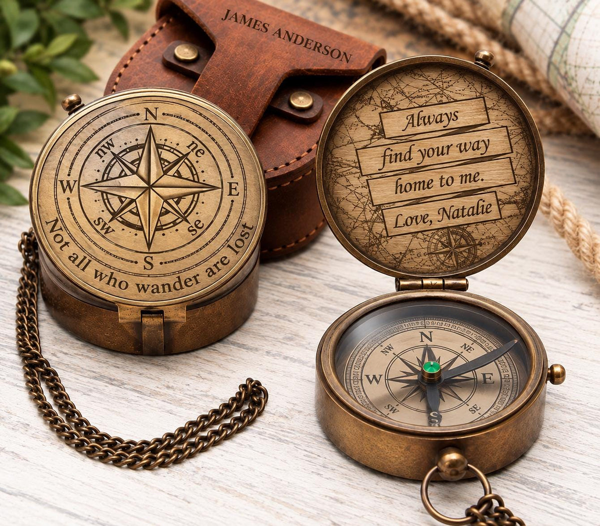 Open and closed views of an engraved brass compass beside a brown leather pouch, showing the compass rose lid, handwritten-style message and directional dial.