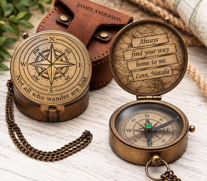 Open and closed views of an engraved brass compass beside a brown leather pouch, showing the compass rose lid, handwritten-style message and directional dial.