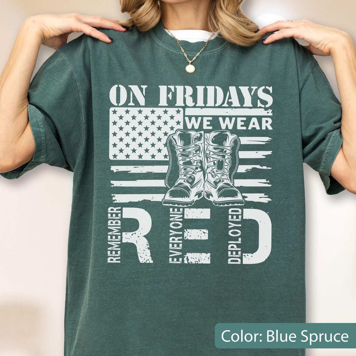 May include: A blue spruce t-shirt featuring a white graphic of an American flag, a pair of military boots, and the text ON FRIDAYS WE WEAR RED REMEMBER EVERYONE DEPLOYED. The shirt has a crew neckline and short sleeves, showcasing a distressed print.