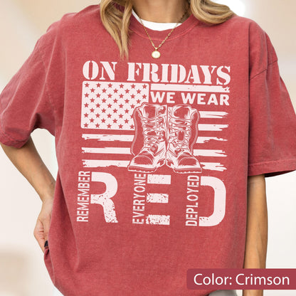 May include: A crimson short-sleeve t-shirt featuring a white graphic of an American flag, a pair of military boots, and the text: ON FRIDAYS WE WEAR RED, REMEMBER EVERYONE DEPLOYED. The shirt has a crew neckline and a relaxed, casual fit.
