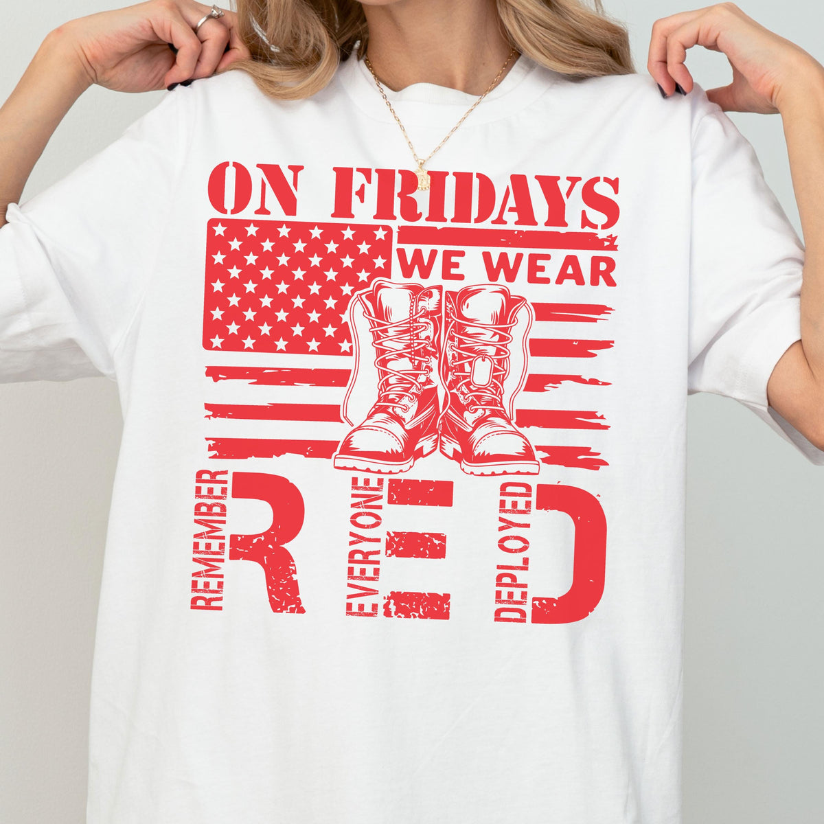 May include: A white short-sleeved t-shirt featuring a red graphic of an American flag, a pair of military boots, and the text ON FRIDAYS WE WEAR RED REMEMBER EVERYONE DEPLOYED. The design is centered on the chest of the garment.