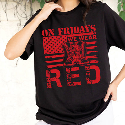 May include: A black short-sleeved t-shirt featuring a red graphic design. The print includes a stylized American flag, a pair of military boots, and the text ON FRIDAYS WE WEAR RED, REMEMBER EVERYONE DEPLOYED in a distressed, bold red font.