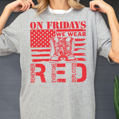 May include: A heather gray t-shirt featuring a red graphic design. The print includes a stylized American flag, a pair of combat boots, and the text: ON FRIDAYS WE WEAR RED, REMEMBER EVERYONE DEPLOYED. The design is centered on the front of the shirt.