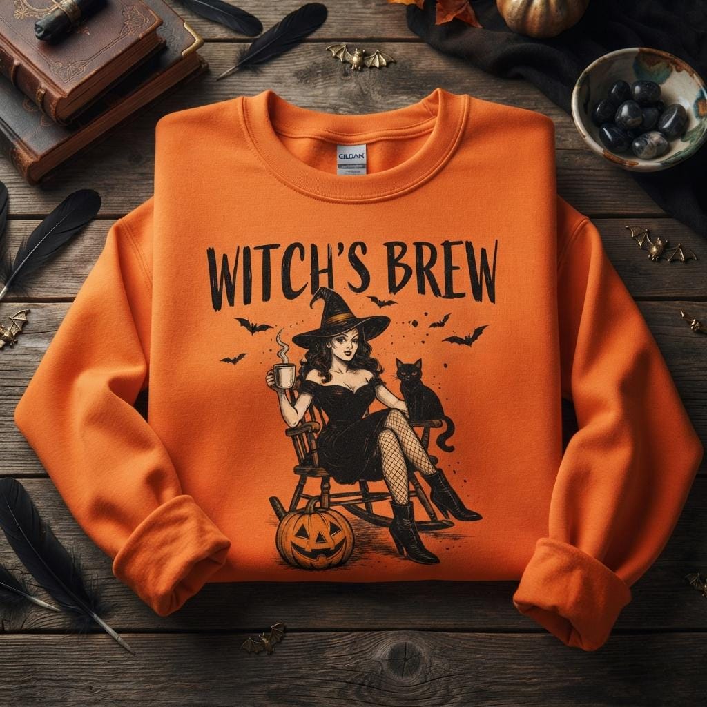 May include: An orange long-sleeve sweatshirt featuring a graphic print of a person in a witch hat sitting in a rocking chair with a black cat, a steaming mug, and a pumpkin. The text "WITCH'S BREW" is printed in black above the illustration.
