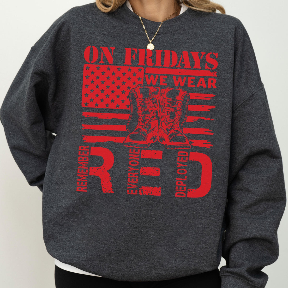 May include: A dark charcoal gray crewneck sweatshirt featuring a red graphic print. The design includes a stylized American flag, a pair of combat boots, and the text: ON FRIDAYS WE WEAR RED, REMEMBER EVERYONE DEPLOYED, arranged in a bold layout.