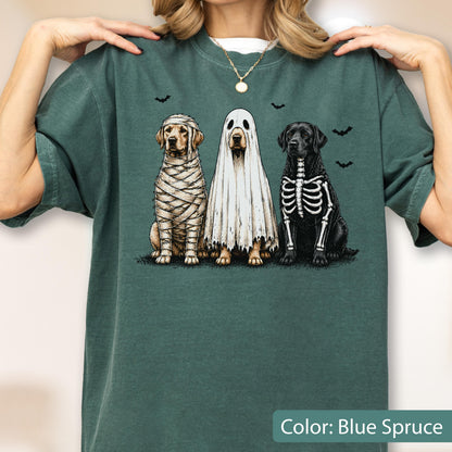 May include: A blue spruce crewneck t-shirt featuring a graphic of three dogs in Halloween costumes: one wrapped like a mummy, one wearing a white ghost sheet, and one with a skeleton print, surrounded by small black bat silhouettes.