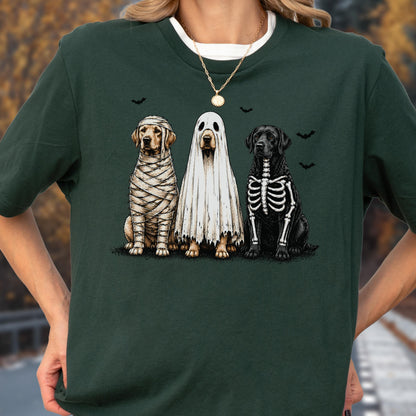 May include: A dark green t-shirt featuring a graphic of three dogs in Halloween costumes. One dog is wrapped like a mummy, one is wearing a white ghost sheet, and one has a skeleton print on its black fur. Small black bats are printed above them.